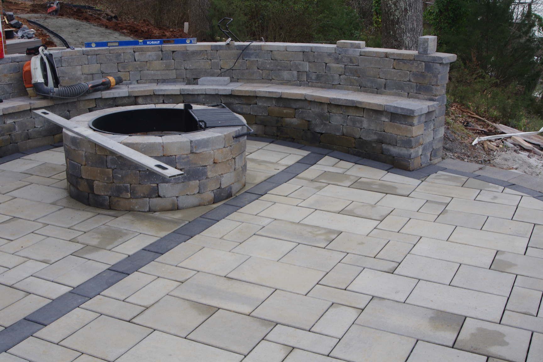 Stone patio with a curved built-in seating wall and round fire pit area under construction
