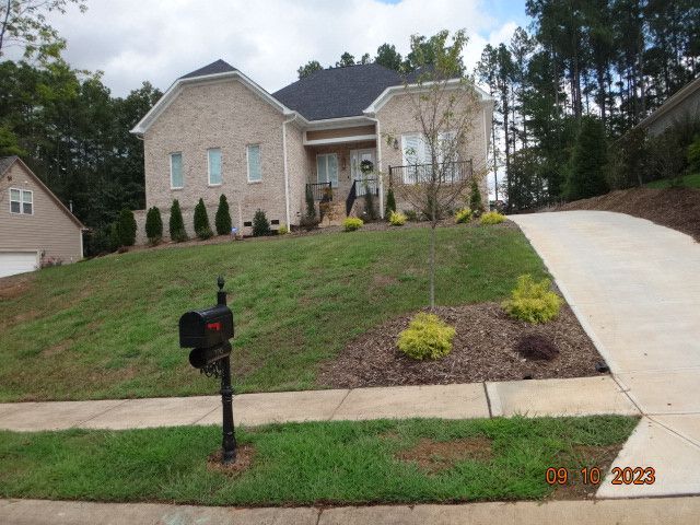 Suburban brick house on a sloped lawn with mailbox and curving driveway.