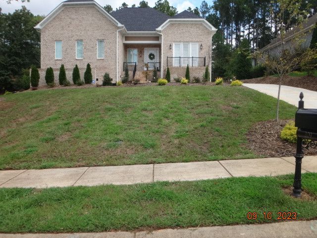 Brick house with a front lawn, shrubs, and a driveway on a sunny day
