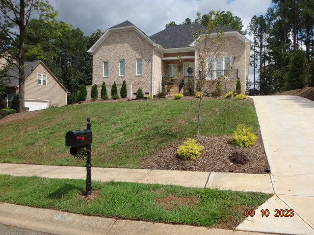 Brick suburban house with a sloped lawn, mailbox, and driveway under cloudy skies