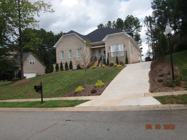 Brick suburban house on a sloped lawn with driveway and mailbox, viewed from the street