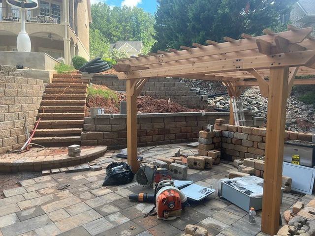 Backyard patio under construction with pergola, brick steps, tools, and stacked materials