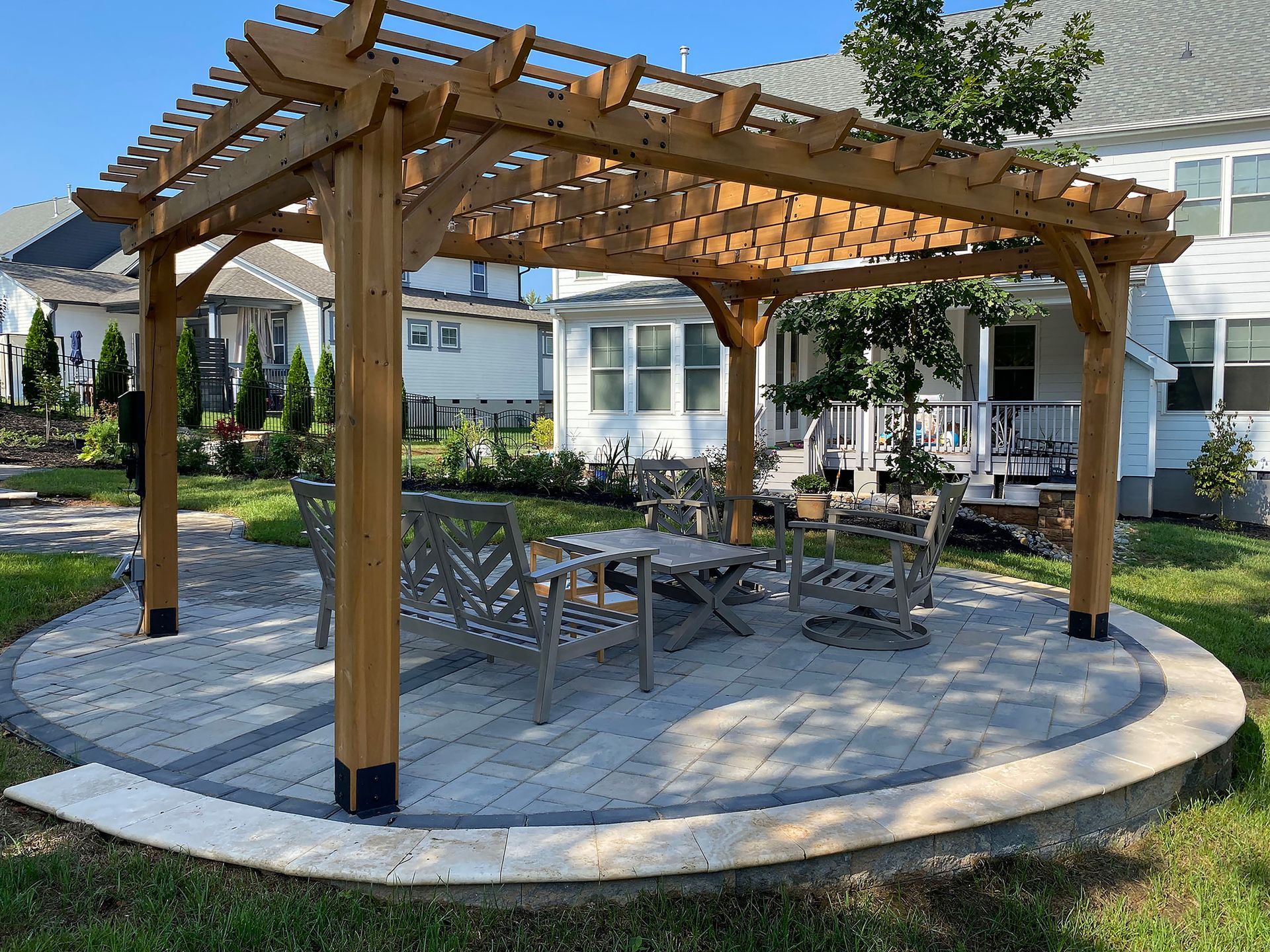 Wooden gazebo with picnic tables on a paved patio in a grassy residential yard