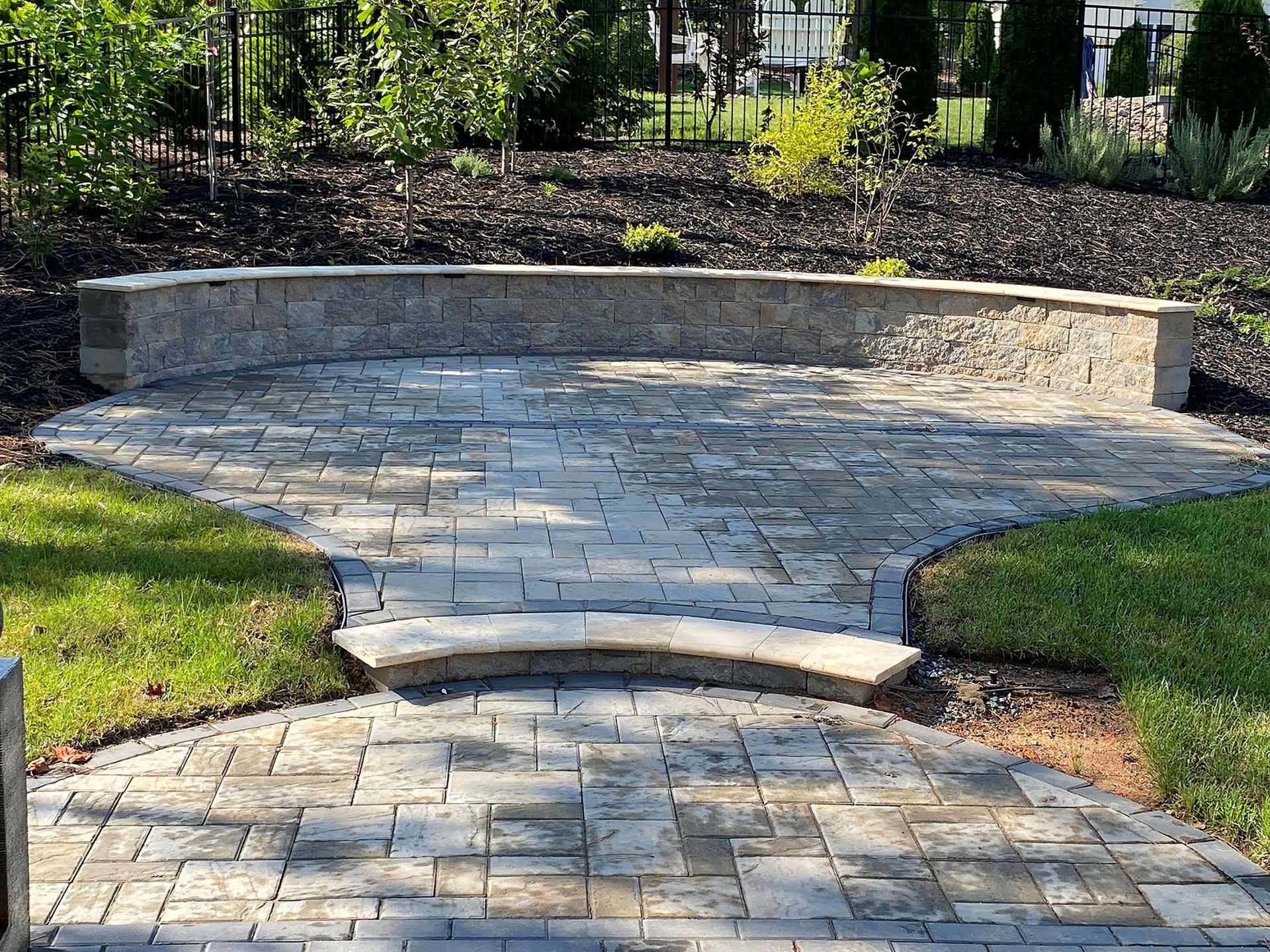 Stone patio with curved steps and a low retaining wall in a landscaped garden
