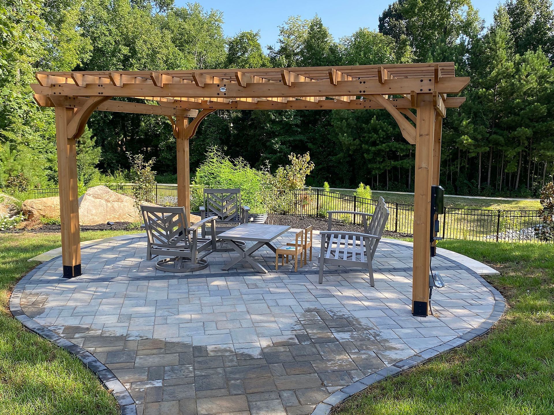 Wooden pergola over a stone patio with metal tables and chairs in a garden setting