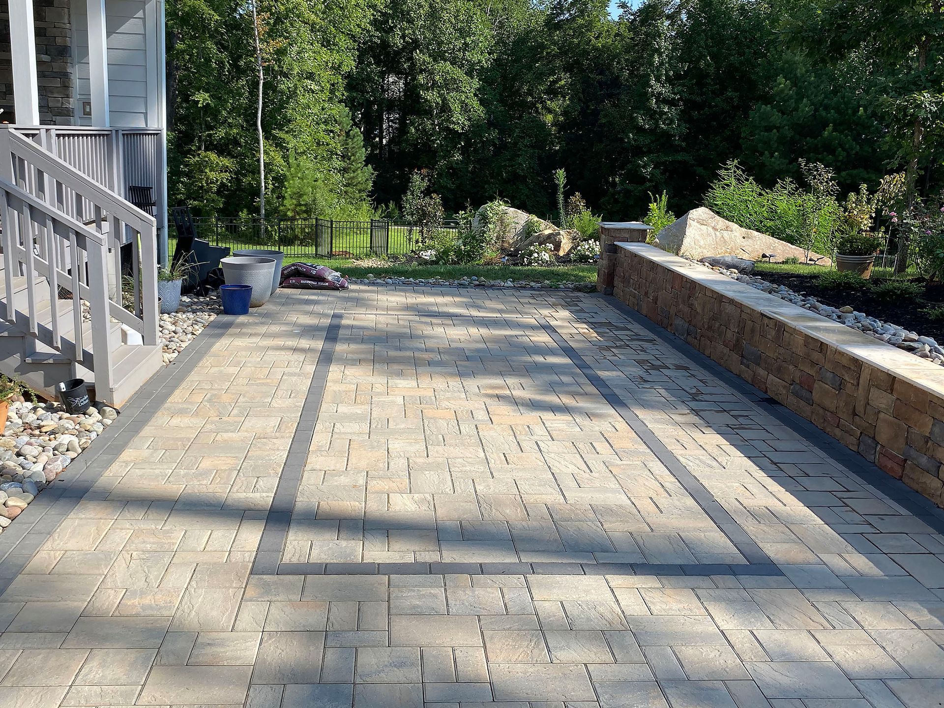 Paved patio with stone border, steps on the left, and trees in the background.