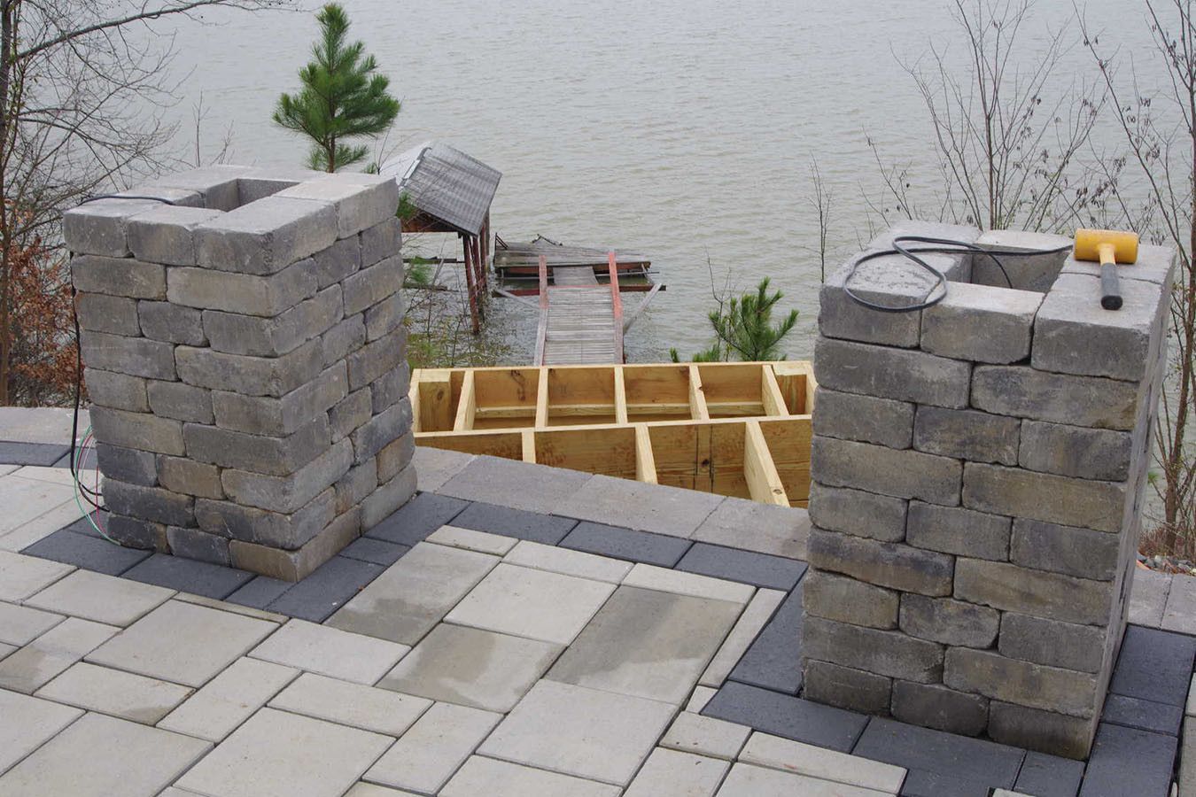 Partially built stone wall with two gray pillars on a paved patio