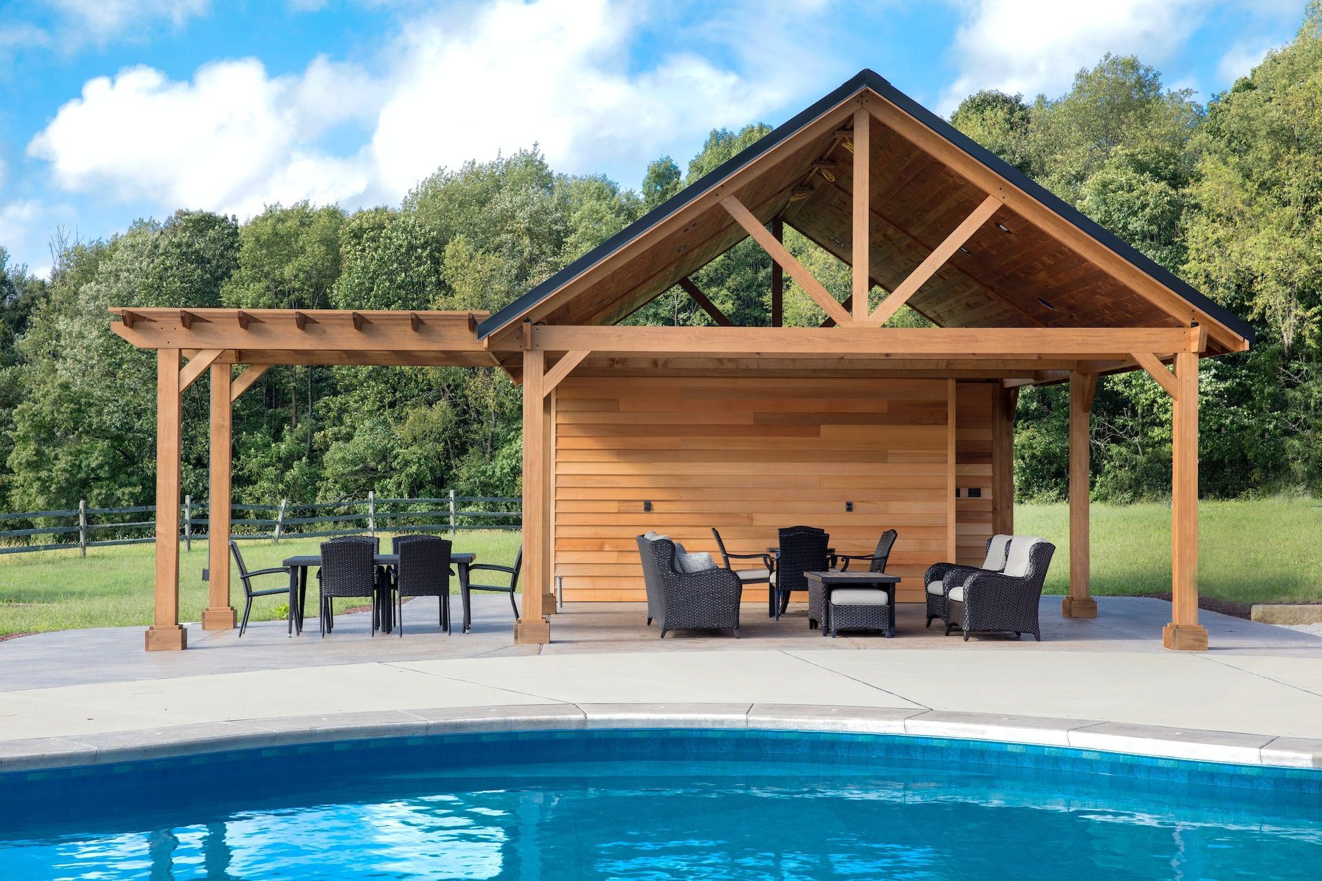 Wooden poolside pavilion with seating and a dining table beside a blue swimming pool