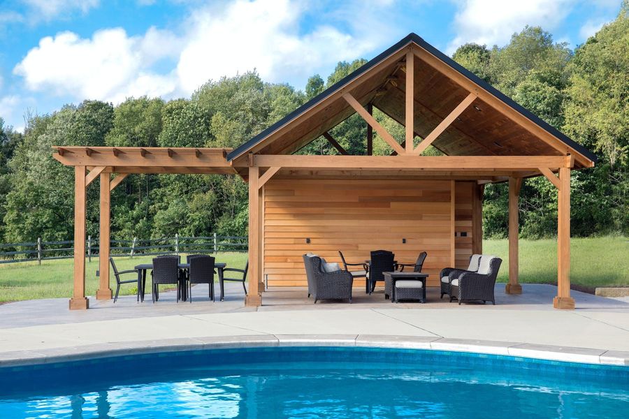 Wooden poolside pavilion with outdoor seating beside a blue swimming pool under a clear sky
