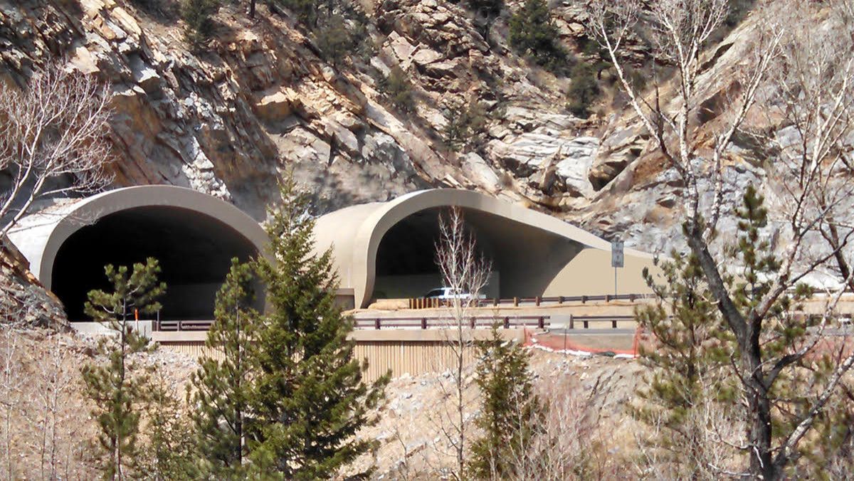 Two tunnel entrances in a rocky hillside above a road, with trees and a metal guardrail in front