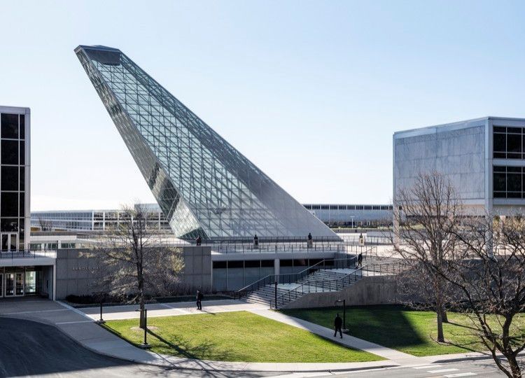 Modern glass building with a tilted atrium over a green courtyard and bare trees