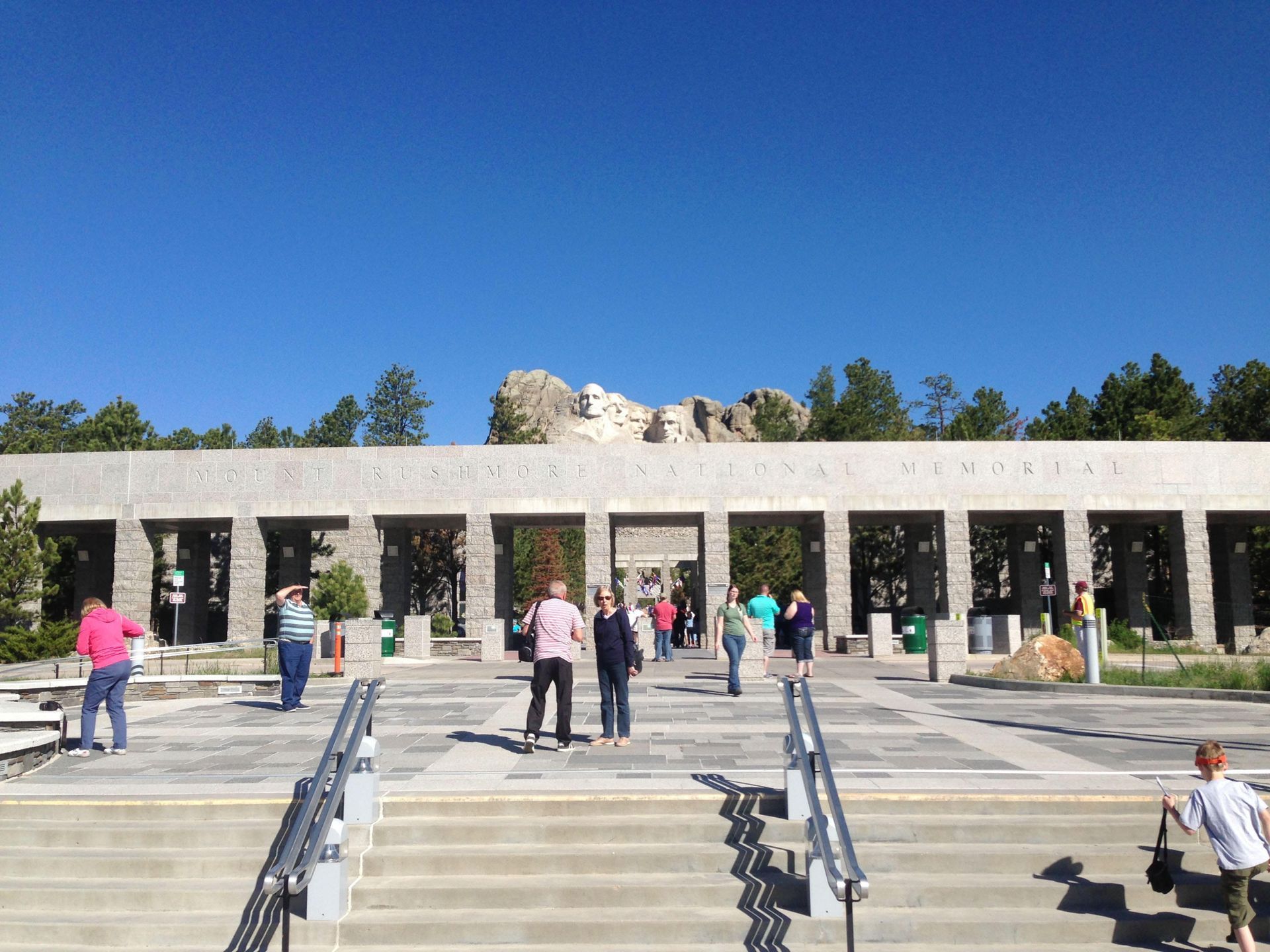 People walking up stairs toward a stone colonnade under a clear blue sky.