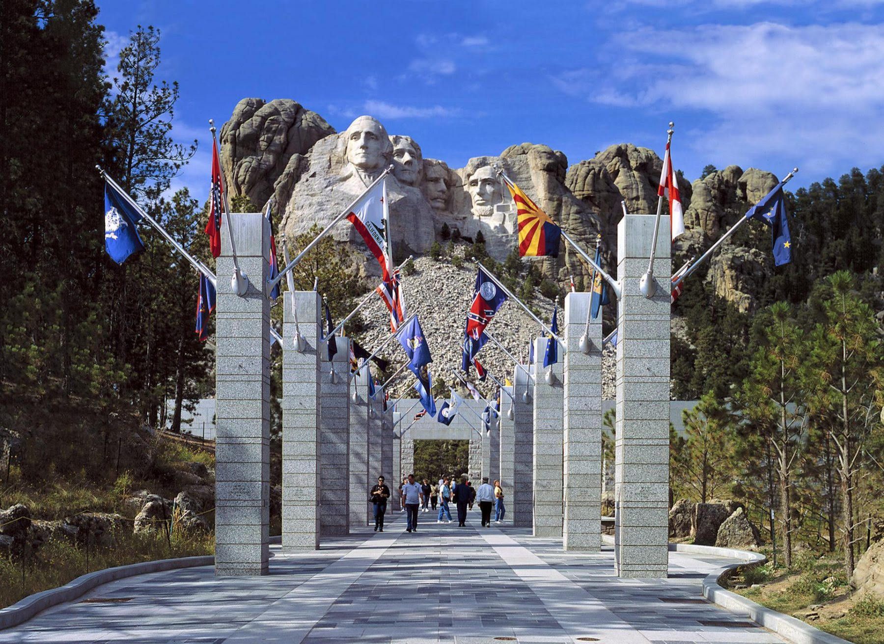 Mount Rushmore framed by a stone archway with hanging flags and a walkway leading toward the monument
