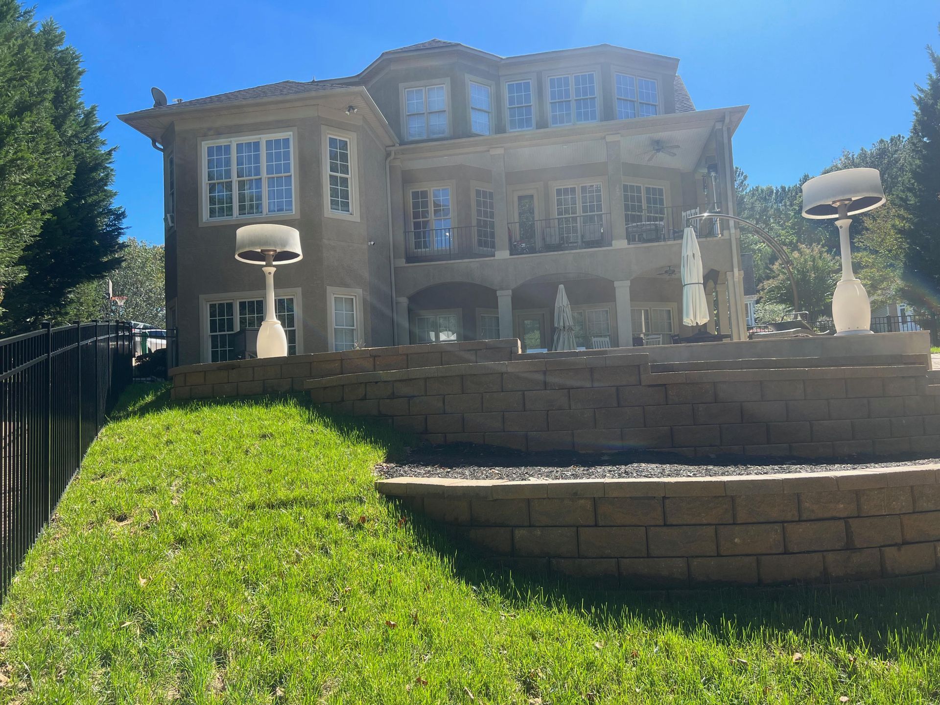 Large beige house with stone steps and a green lawn under a bright blue sky