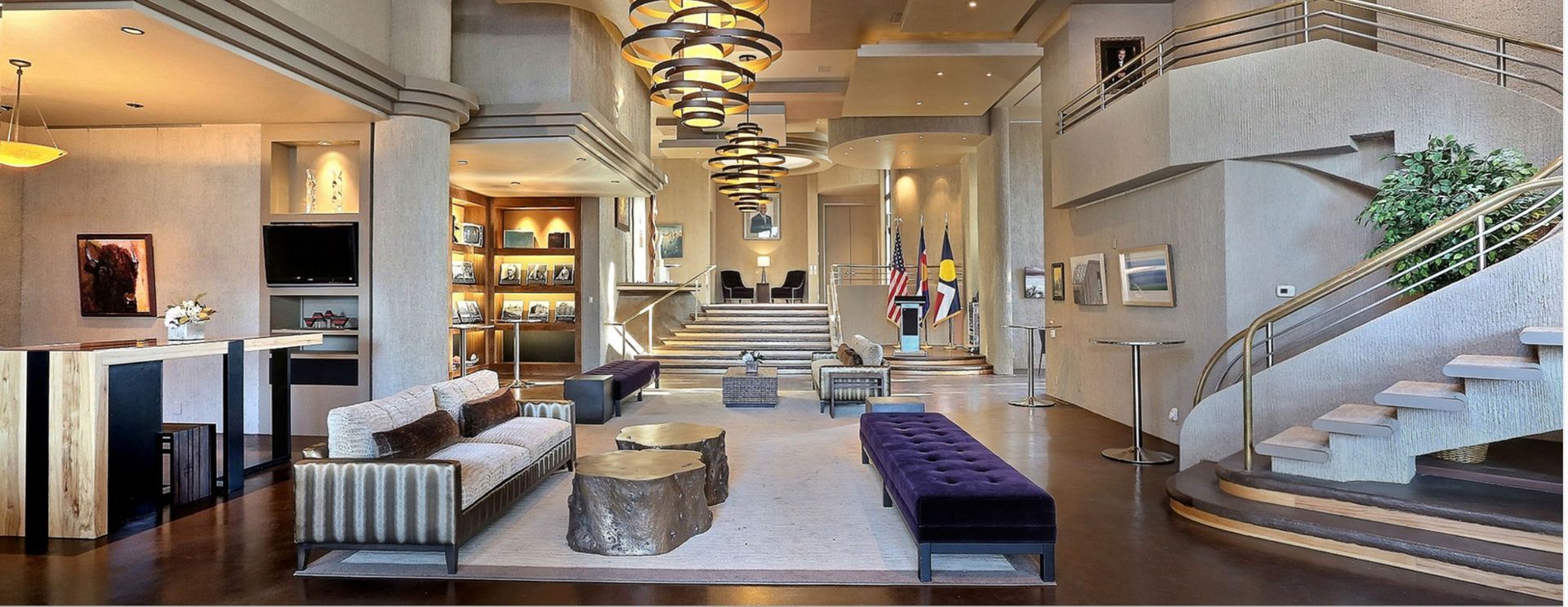 Modern hotel lobby with chandeliers, white seating, marble floors, and a curved staircase