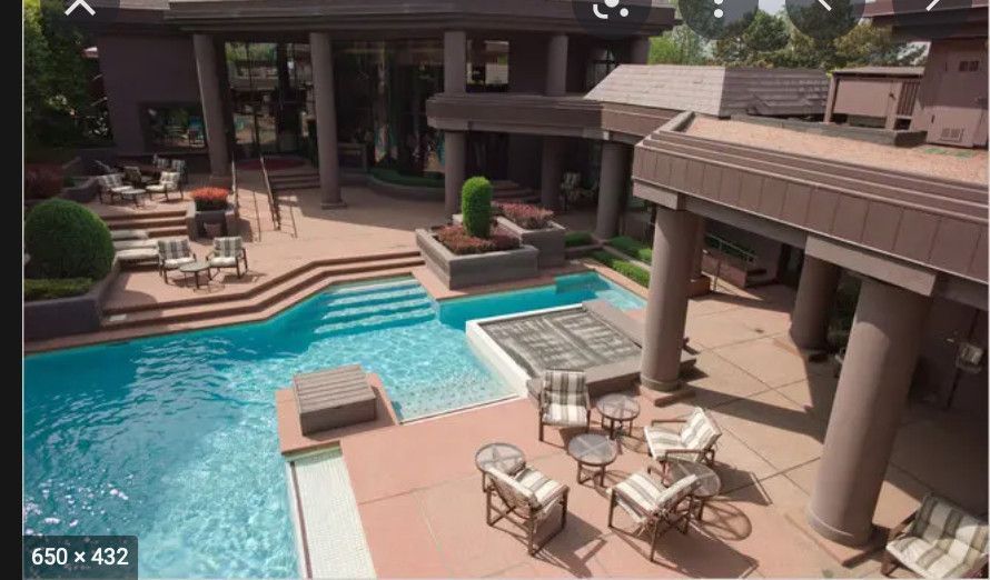 Luxury resort pool with tan loungers, patio umbrellas, and a spa-style water feature