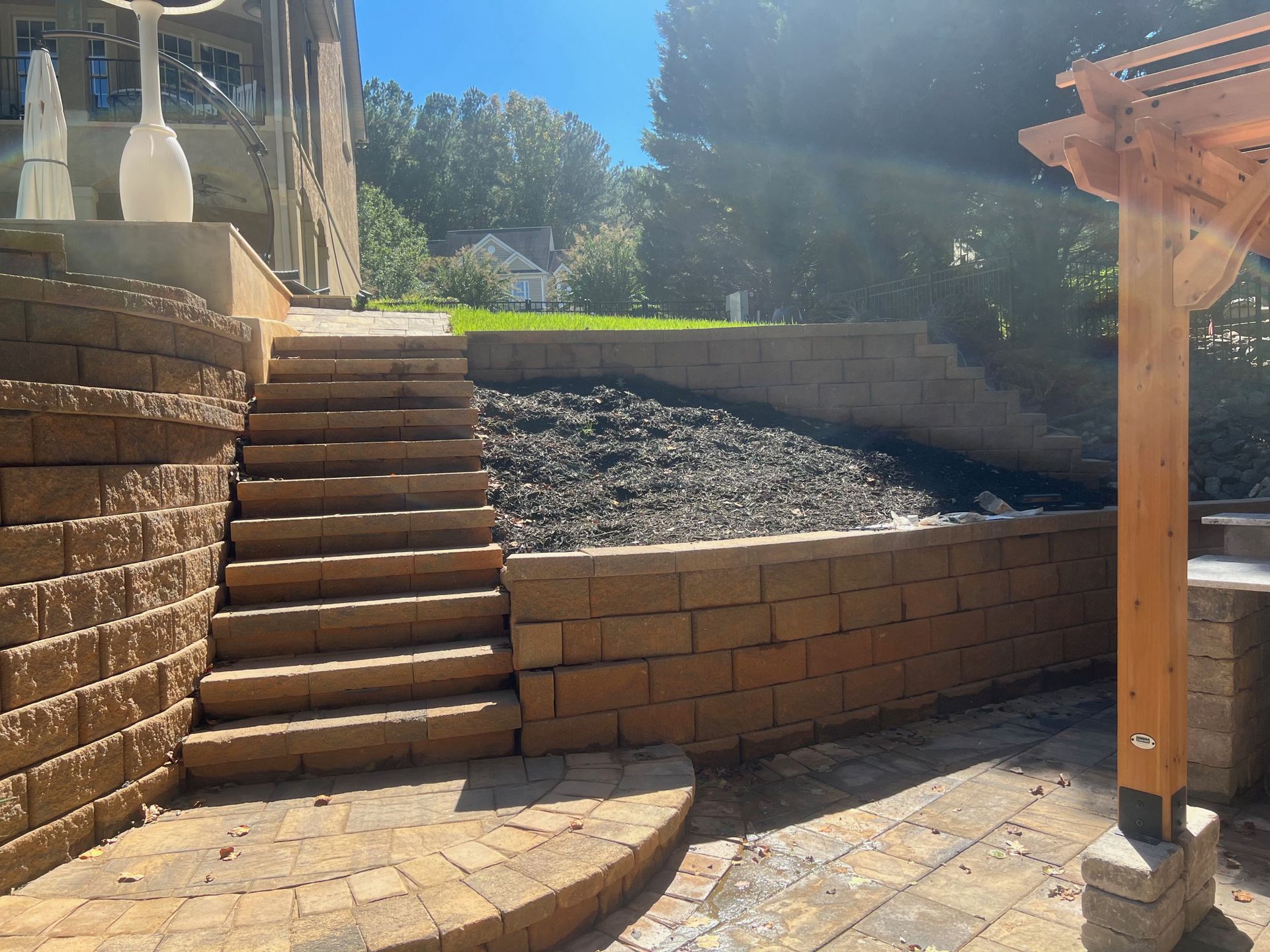 Stone patio steps beside a brick retaining wall and gravel bed in a sunny backyard