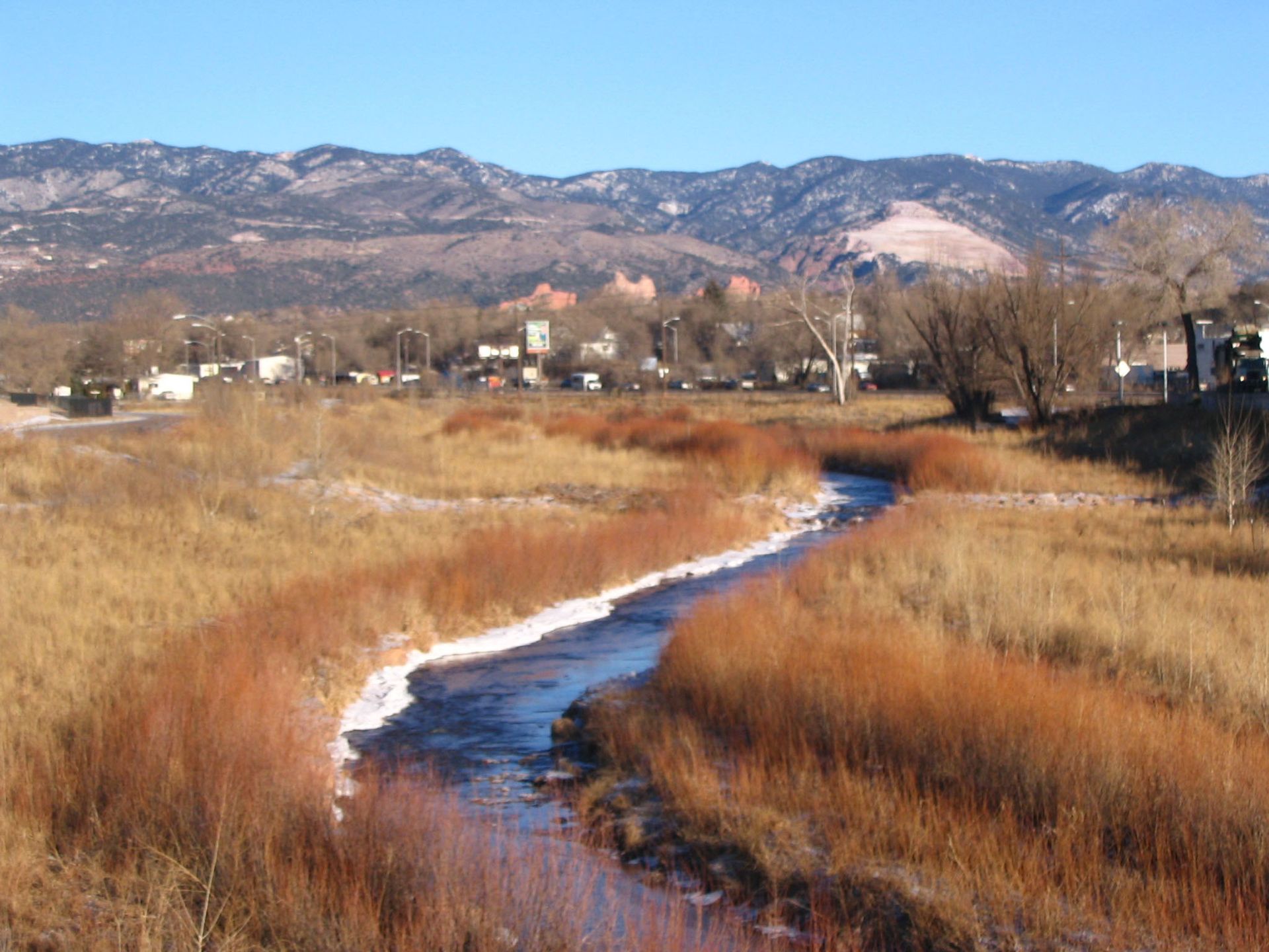 Winding creek through golden marsh grasses with snowy mountains and a distant town under a clear sky