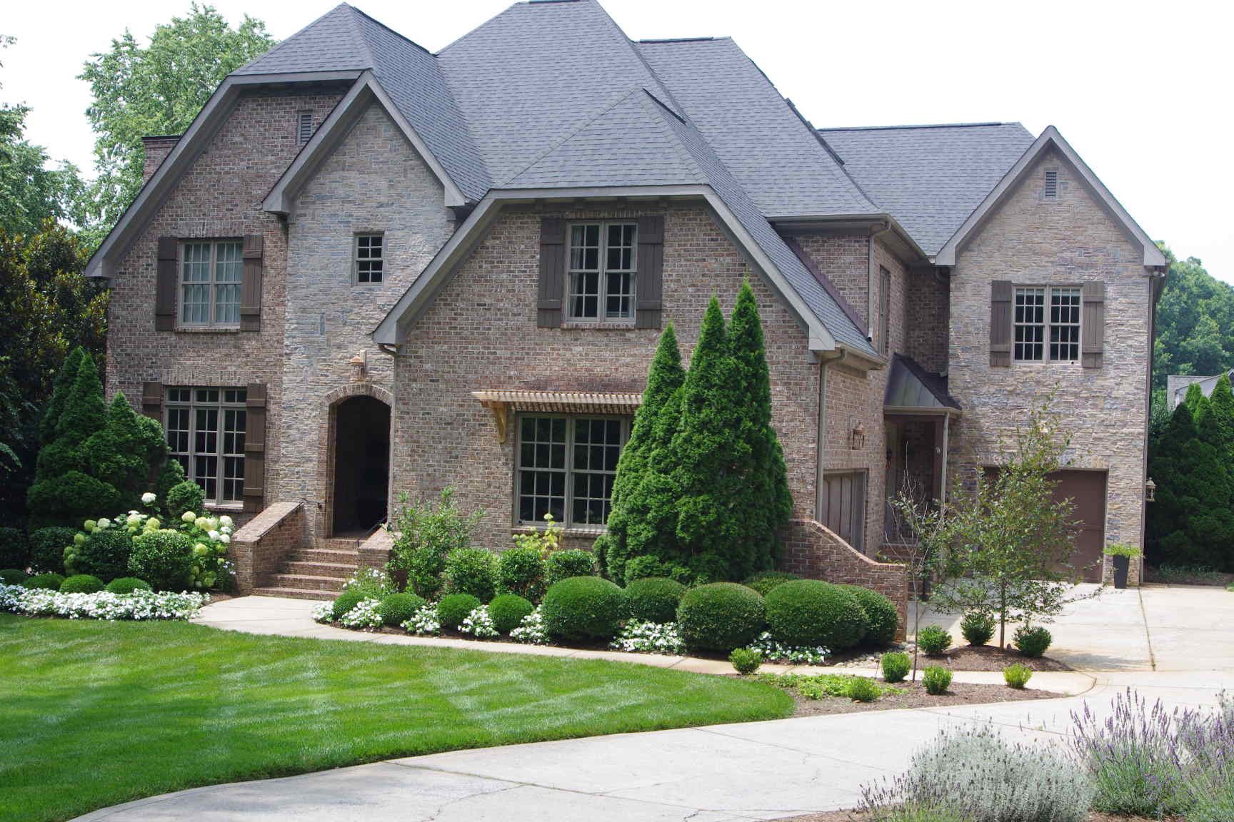 Large stone suburban house with a gabled roof, landscaped front yard, and curved driveway