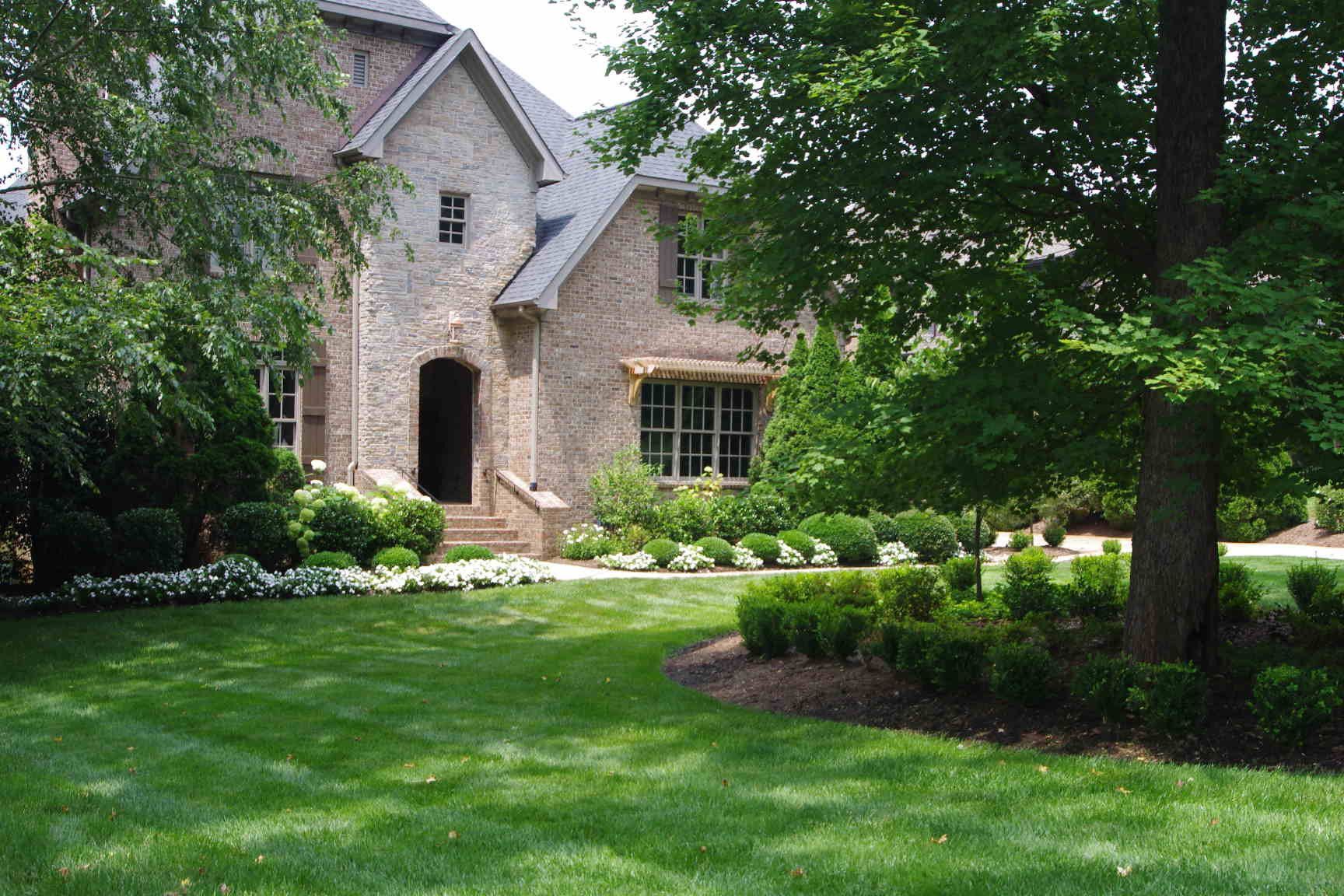 Stone house with arched doorway and manicured lawn surrounded by trees and shrubs