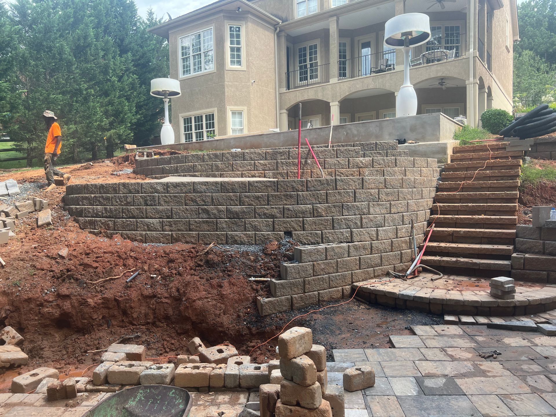 Paved backyard patio with stone border, stairs on the left, and trees in the background.