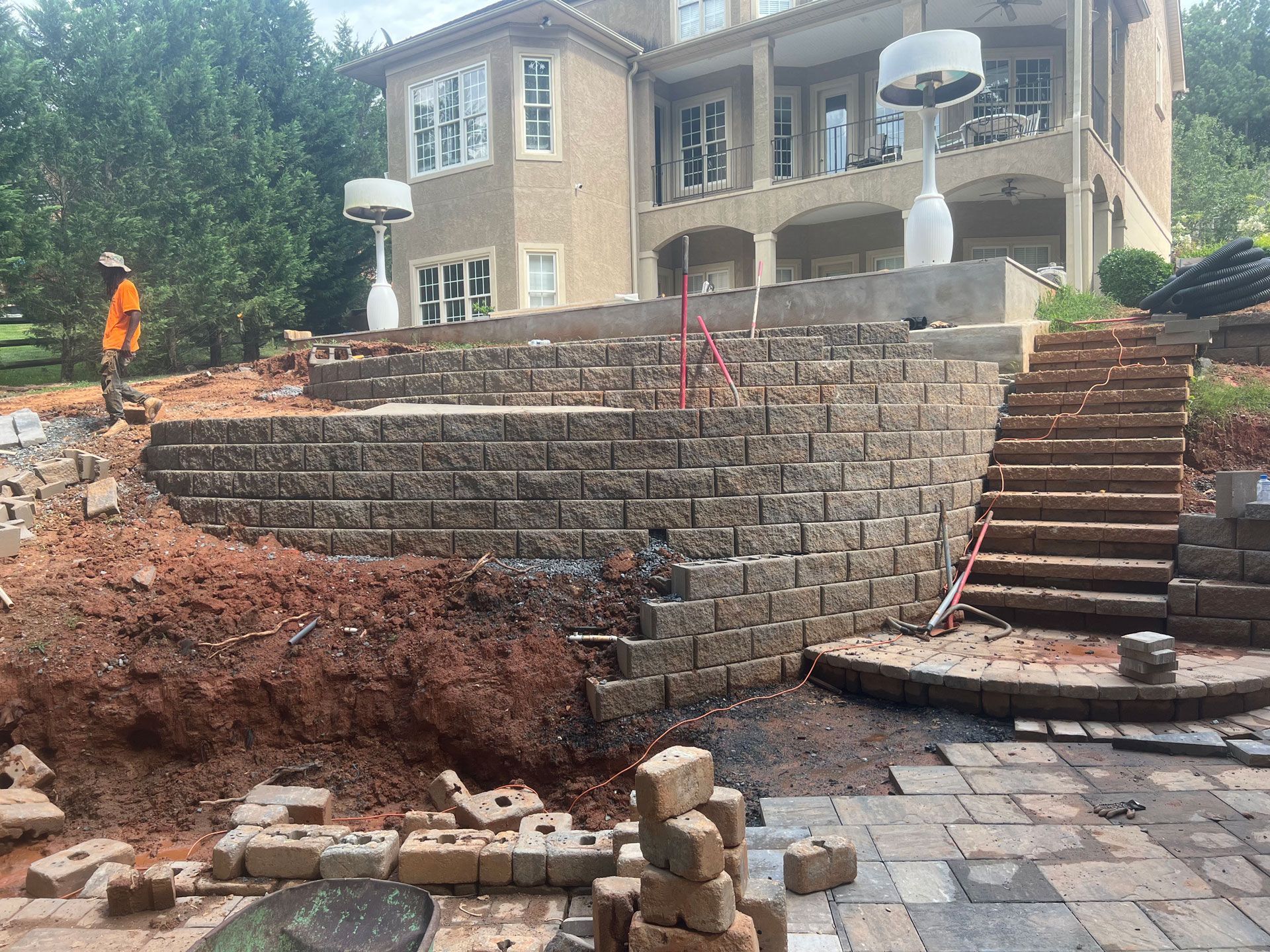 House under construction with stone retaining wall, stairs, and workers at the site