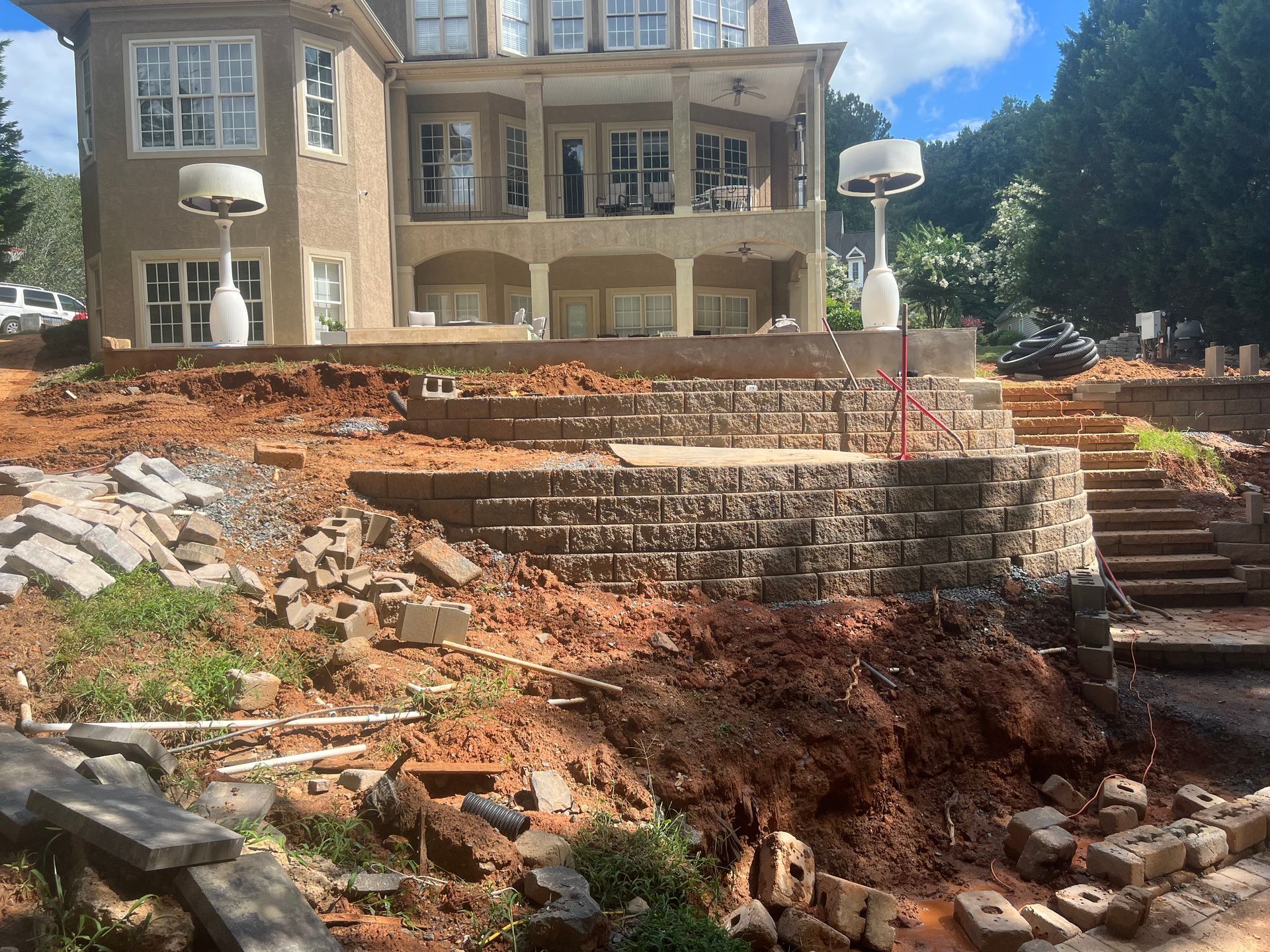 Large house above a steep, partly built stone retaining wall and dirt excavation site