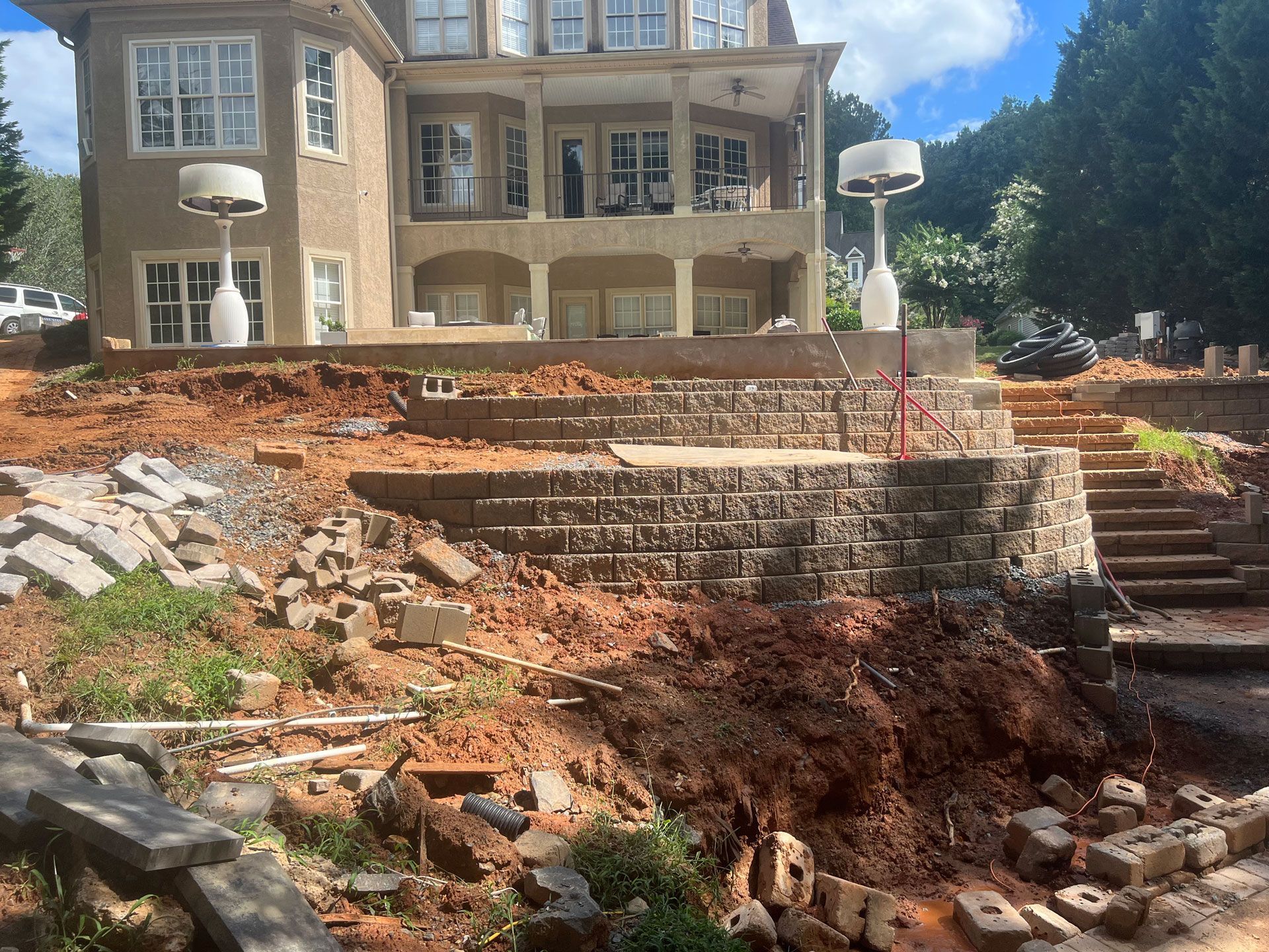 Large house on a hillside with exposed dirt and stone retaining walls under construction.