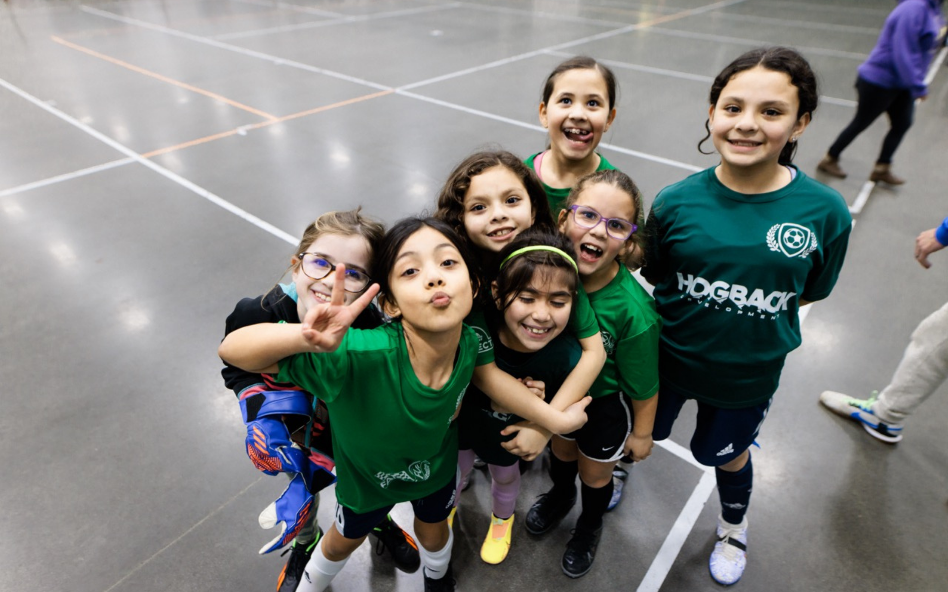 Group of children in green jerseys posing together on an indoor gym floor