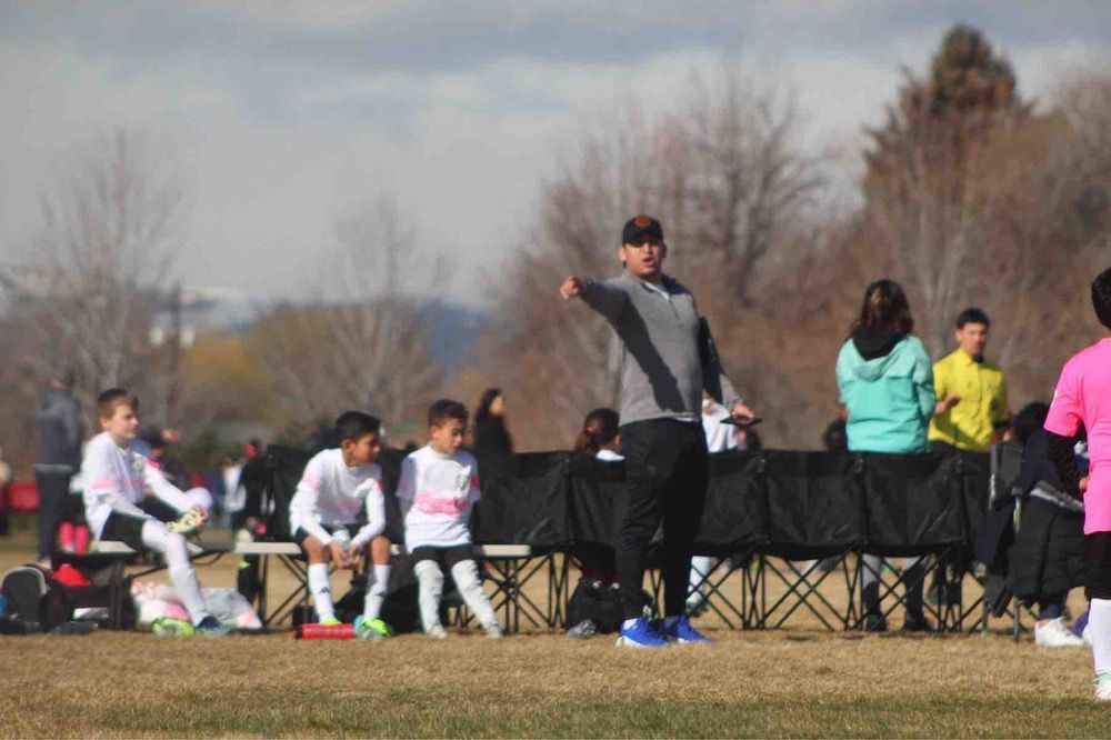 Soccer sideline with seated players and a coach gesturing on a grassy field