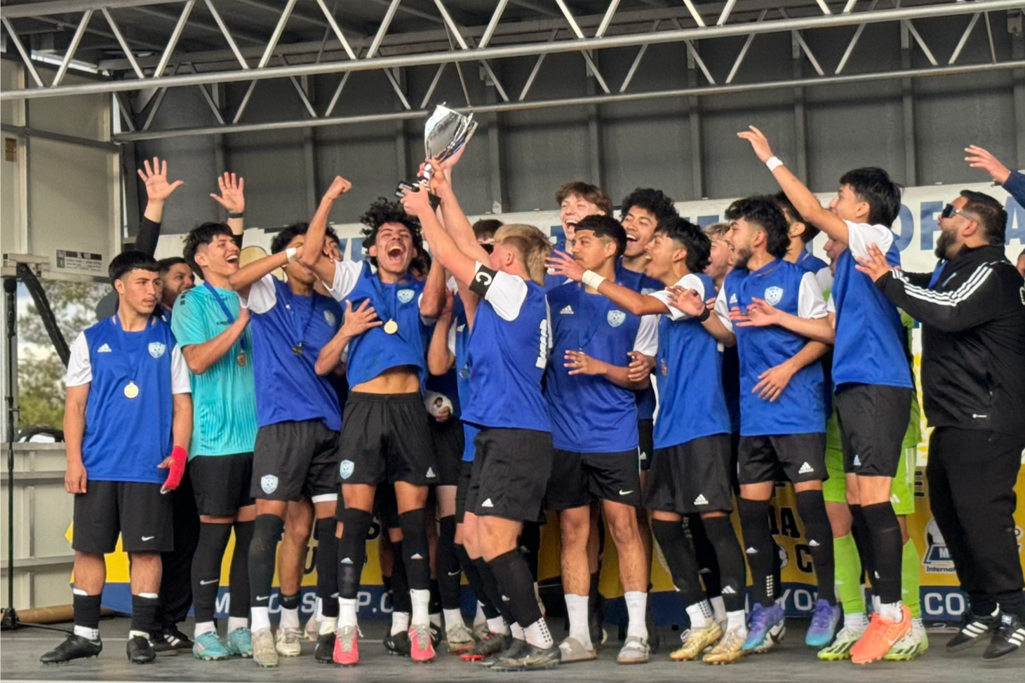 Soccer team in blue jerseys celebrating on a stage, raising hands and cheering together