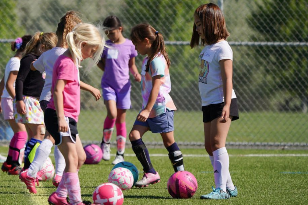 Children practicing soccer drills on a grassy field with pink and purple soccer balls