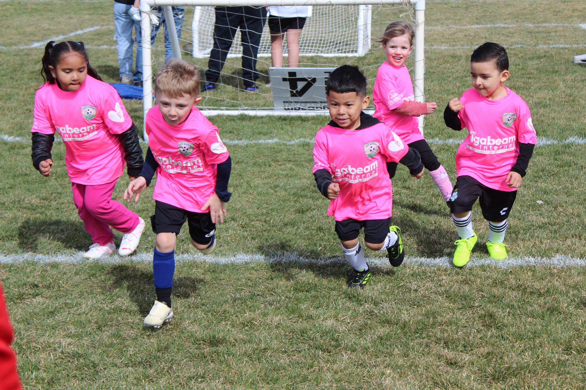 Children in pink jerseys running on a grassy soccer field during a game