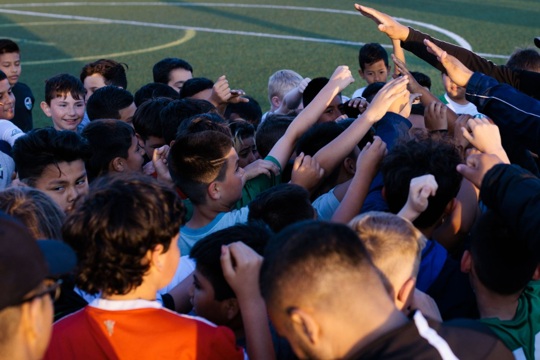 Crowd of soccer players and coaches huddling with raised hands on a field