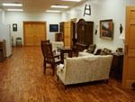 A wide-angle view of a room with wood flooring, featuring a light-colored sofa, dark wood chairs, and wood double doors.