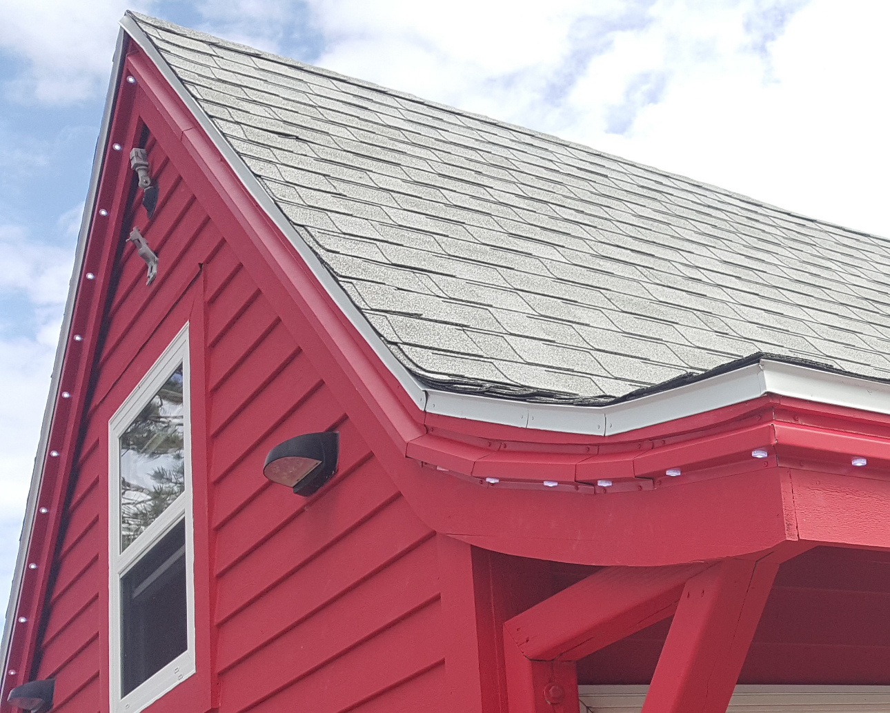 Red building with gray roof, white-framed window, and decorative lights along the eaves.