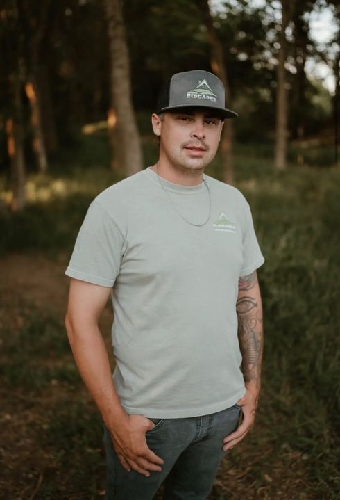 Man in gray shirt and cap smiles in front of red and yellow plants.