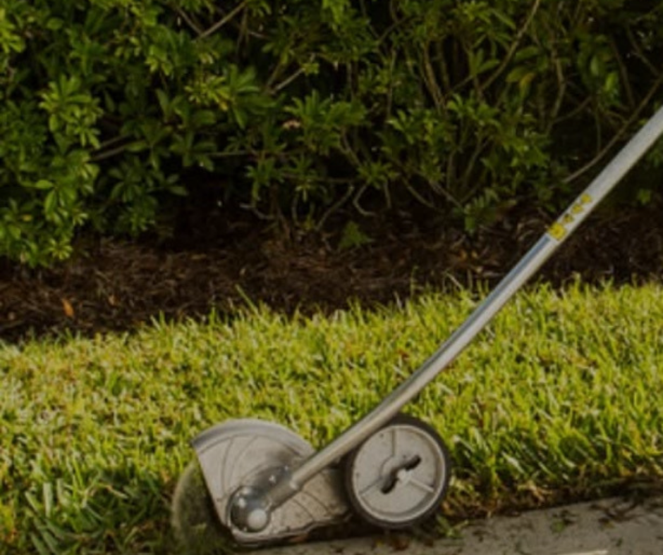 Weed trimmer edging grass next to a dark mulch bed and bushes.