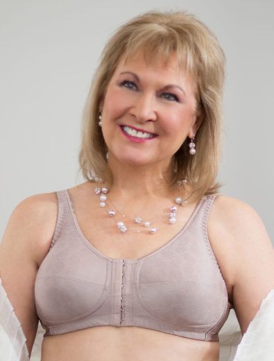 Woman in beige front-closure bra smiles, wearing pearl necklace and earrings.