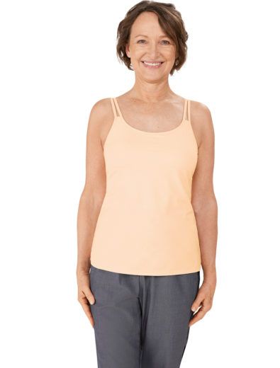 Woman in peach camisole and gray pants smiling.