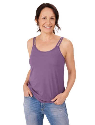 Woman smiling, wearing purple tank top and jeans, hands in pockets.