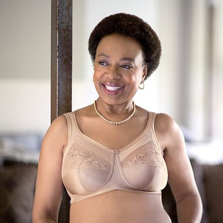 Woman wearing a beige bra, smiling, leaning against a metal post.
