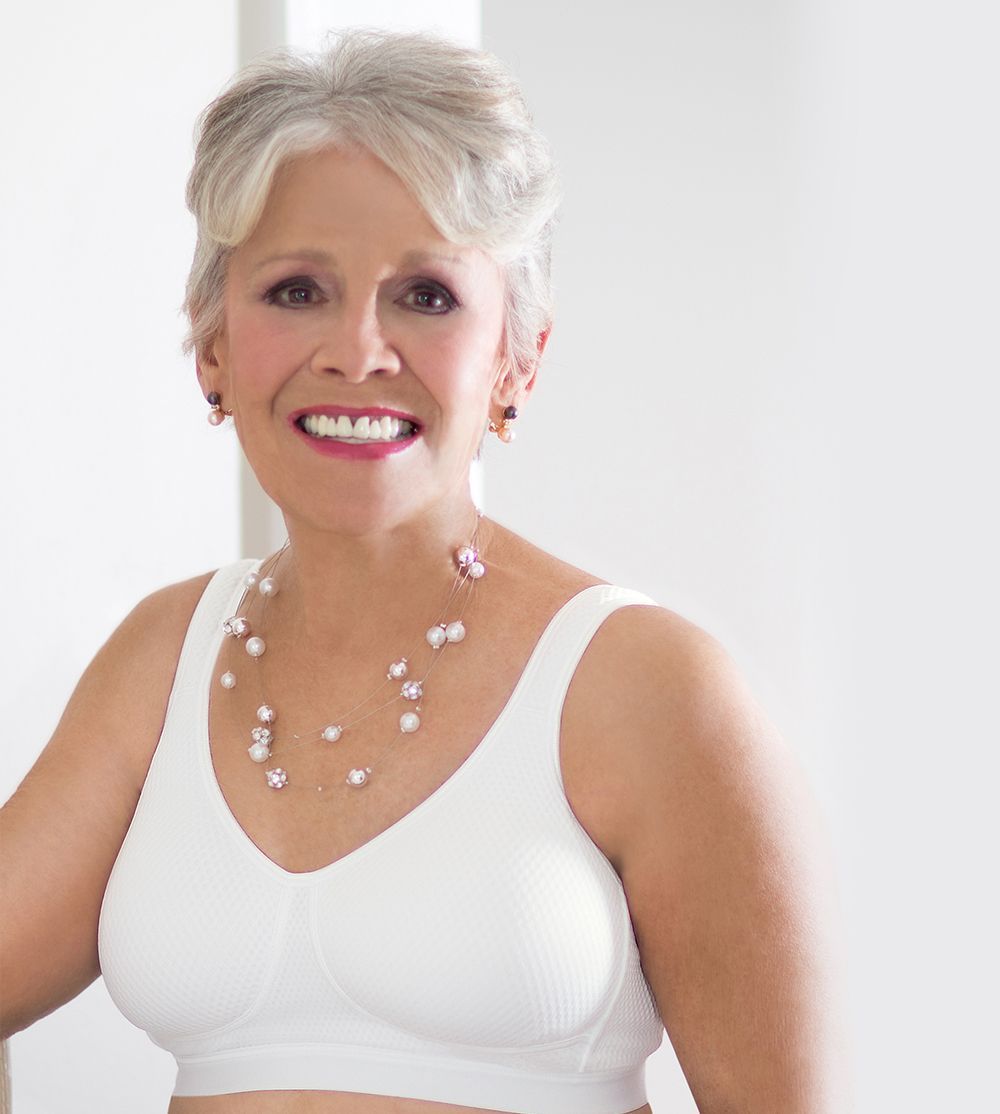 Woman wearing a white, supportive bra, smiling, pearl necklace.