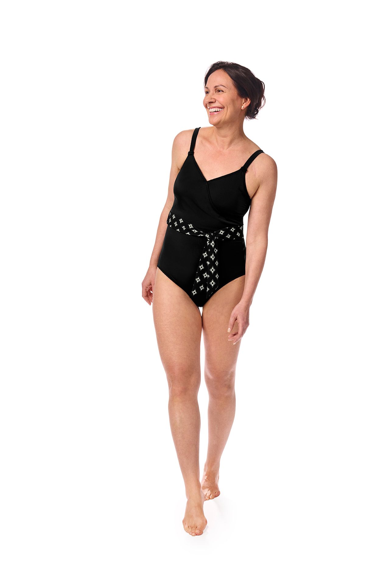 Woman wearing black one-piece swimsuit, smiling, walking forward on a white background.