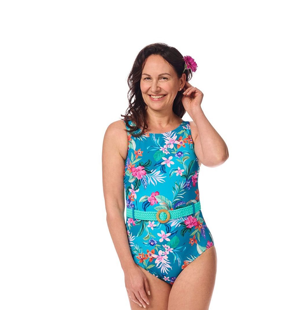 Woman in turquoise floral swimsuit with belt, smiling. Pink flower in hair.