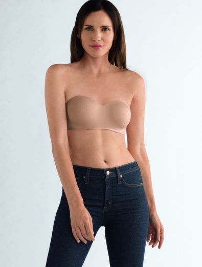 Woman in strapless bra and dark jeans, standing against a white backdrop.