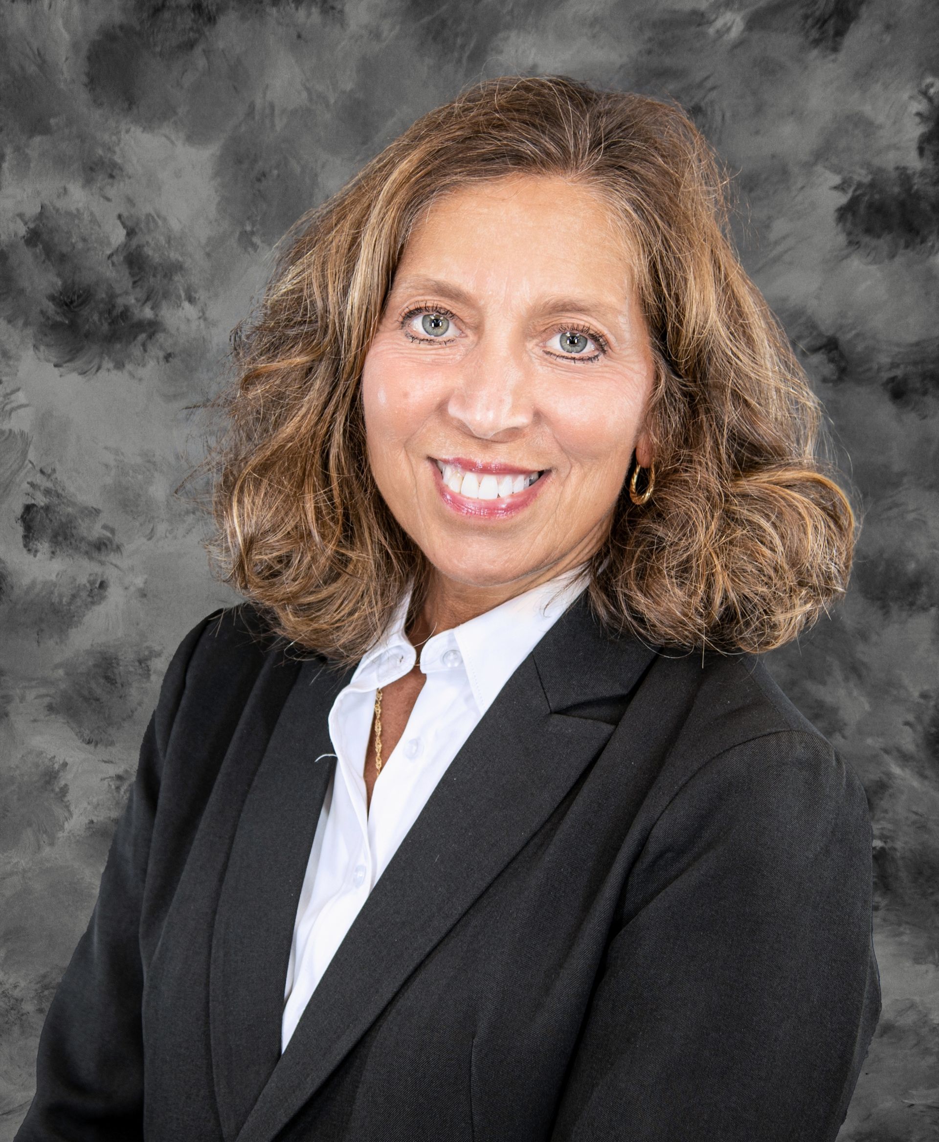 Woman in business suit smiling, posed in front of a gray mottled background.