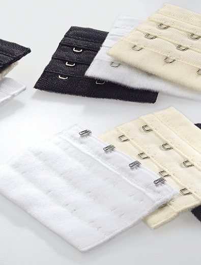 Bra extenders in black, white, and beige with hook-and-eye closures, arranged on a white surface.