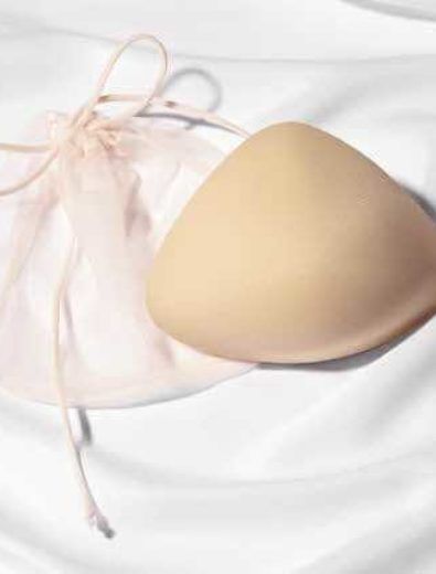 A beige breast prosthesis next to a drawstring bag on a white sheet.