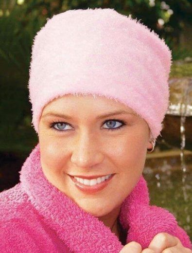Woman with blue eyes wearing a pink fuzzy hat and robe, smiling outdoors.